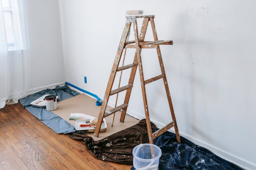 Texto ALT: Interior room prepared for professional wall painting with ladder and protected hardwood floor