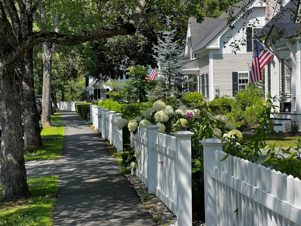 White residential fence along a landscaped front yard and sidewalk